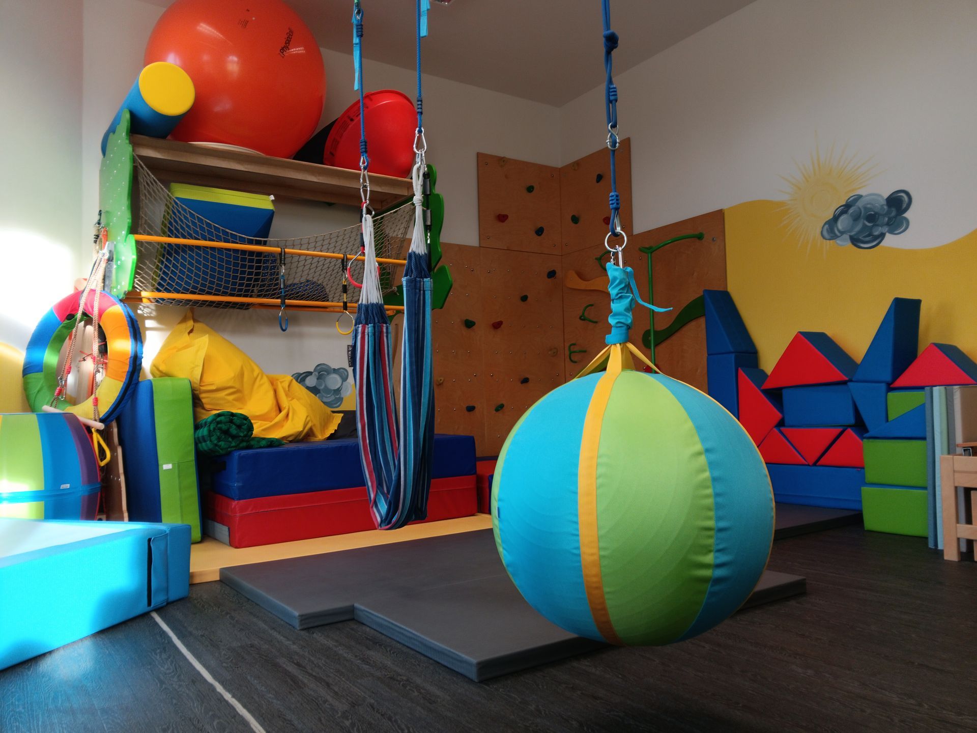 Spielzimmer mit Hängeschaukel, Kletterwand, bunten Bauklötzen und Gymnastikball.