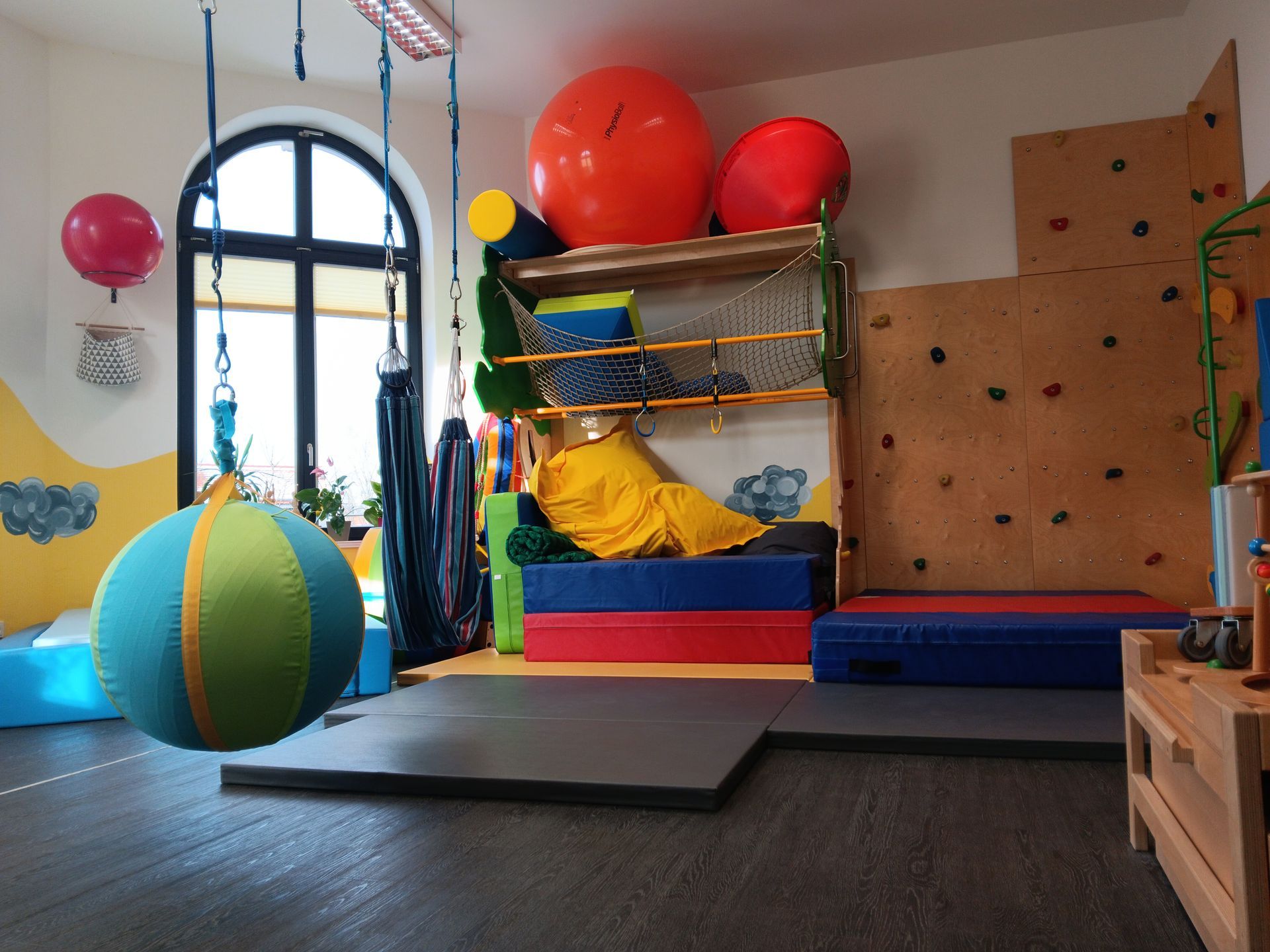 Indoor-Spielbereich mit Kletterwand, Hängeschaukel und bunten Matten.