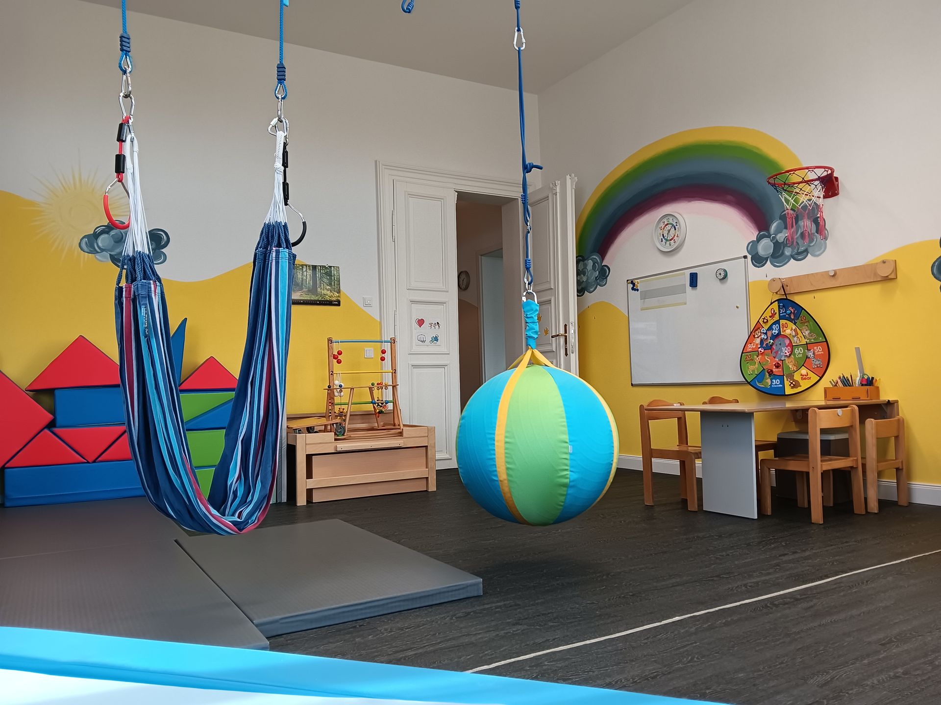 Spielzimmer mit Schaukeln, bunten Wänden und einem kleinen Tisch.
