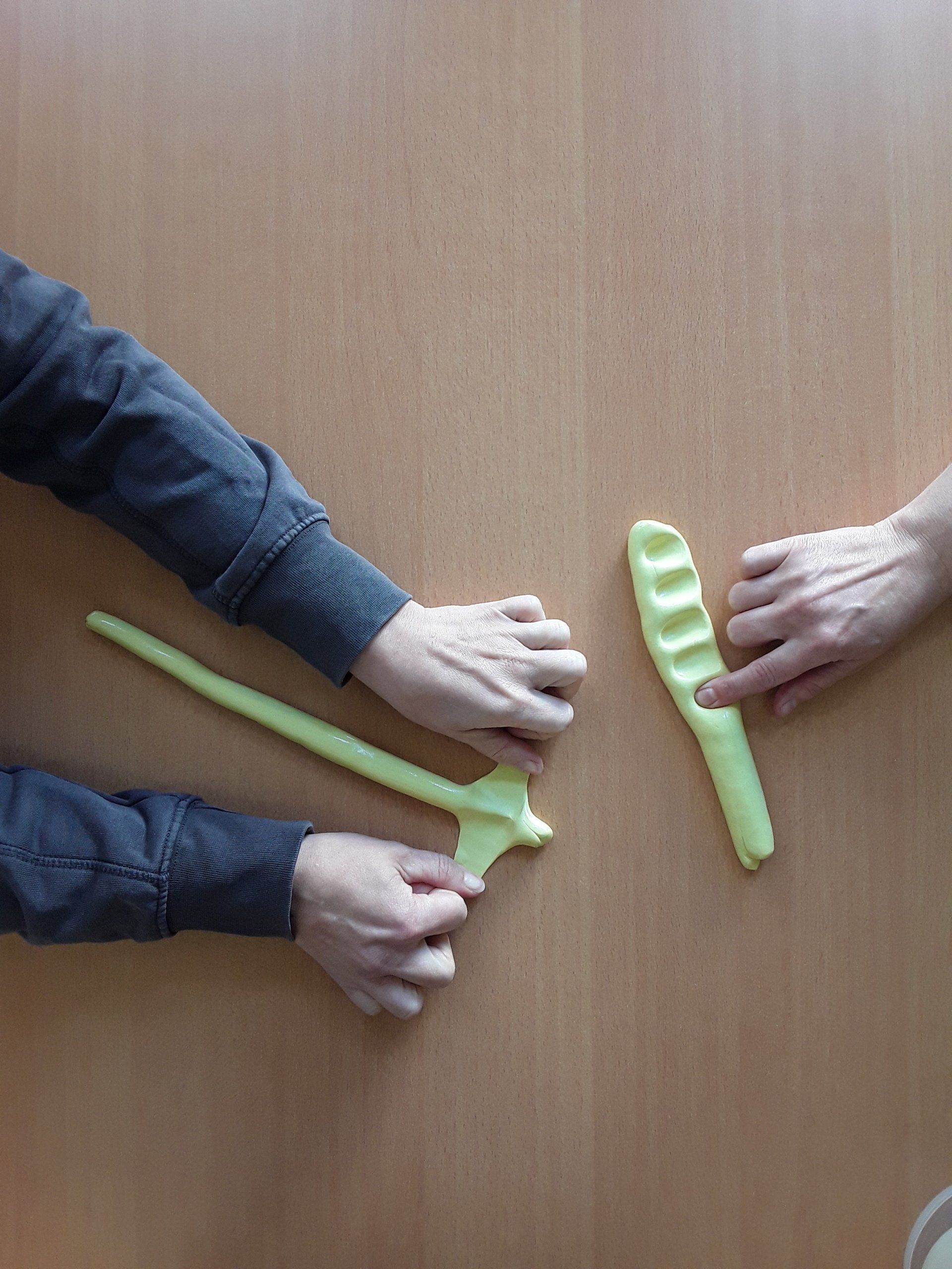 Zwei Personen formen gelben Ton auf einem hellbraunen Tisch; eine Person zeigt, die andere hält ein geformtes Stück.