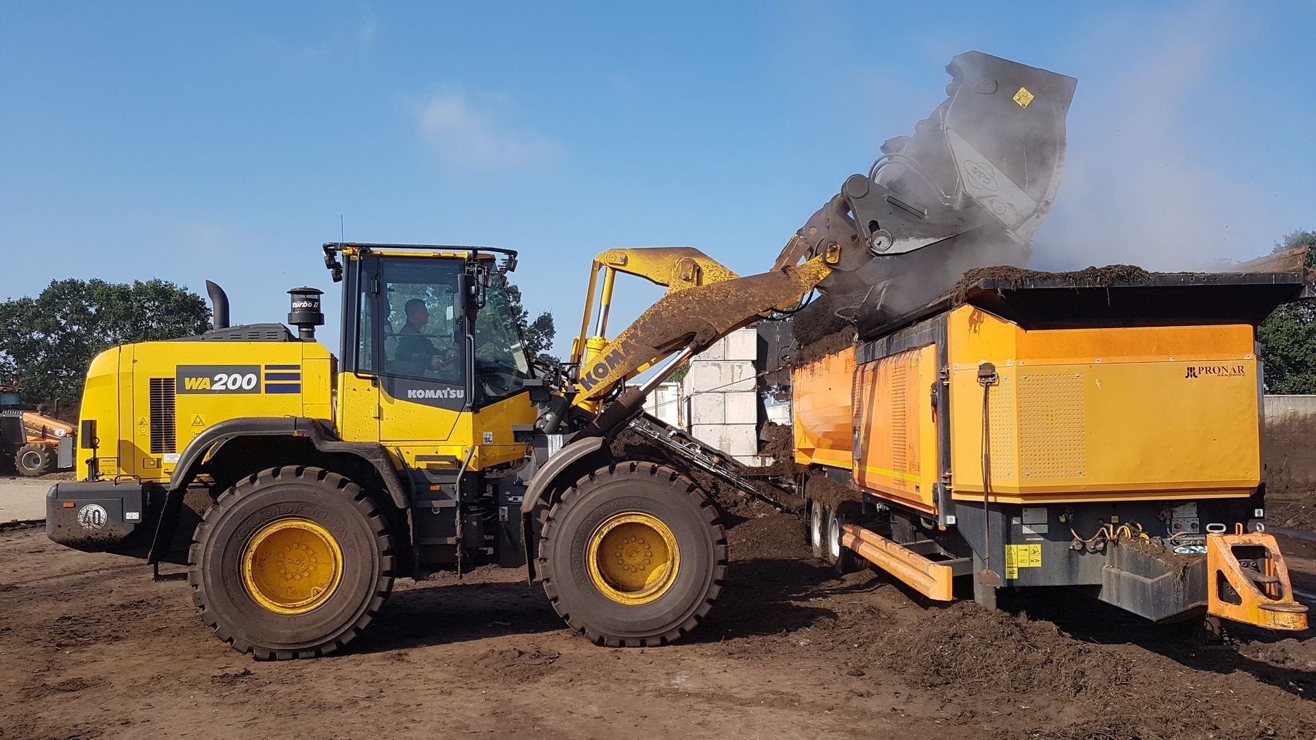 Ein gelber Komatsu lädt Erde in einen Muldenkipper.