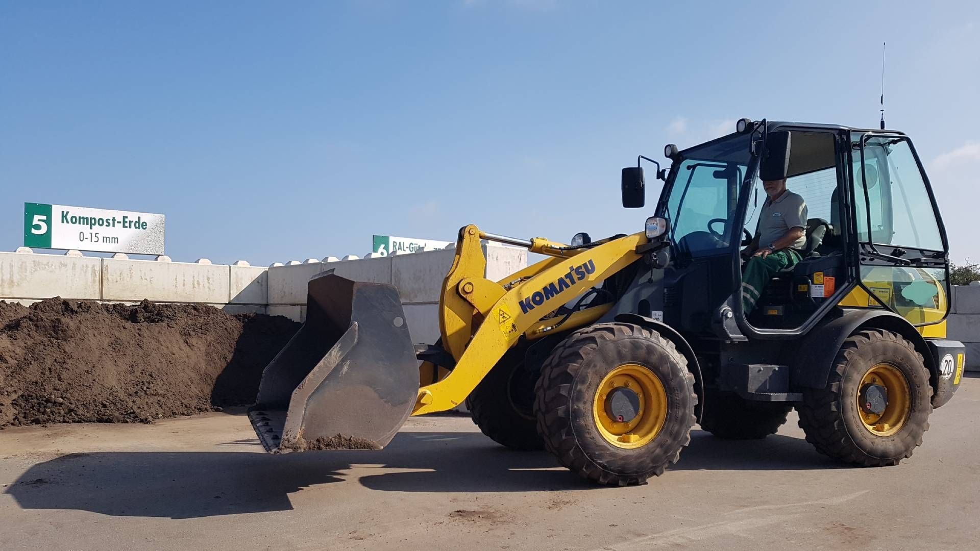 Ein gelb-schwarzer Traktor steht vor einem Erdhaufen.