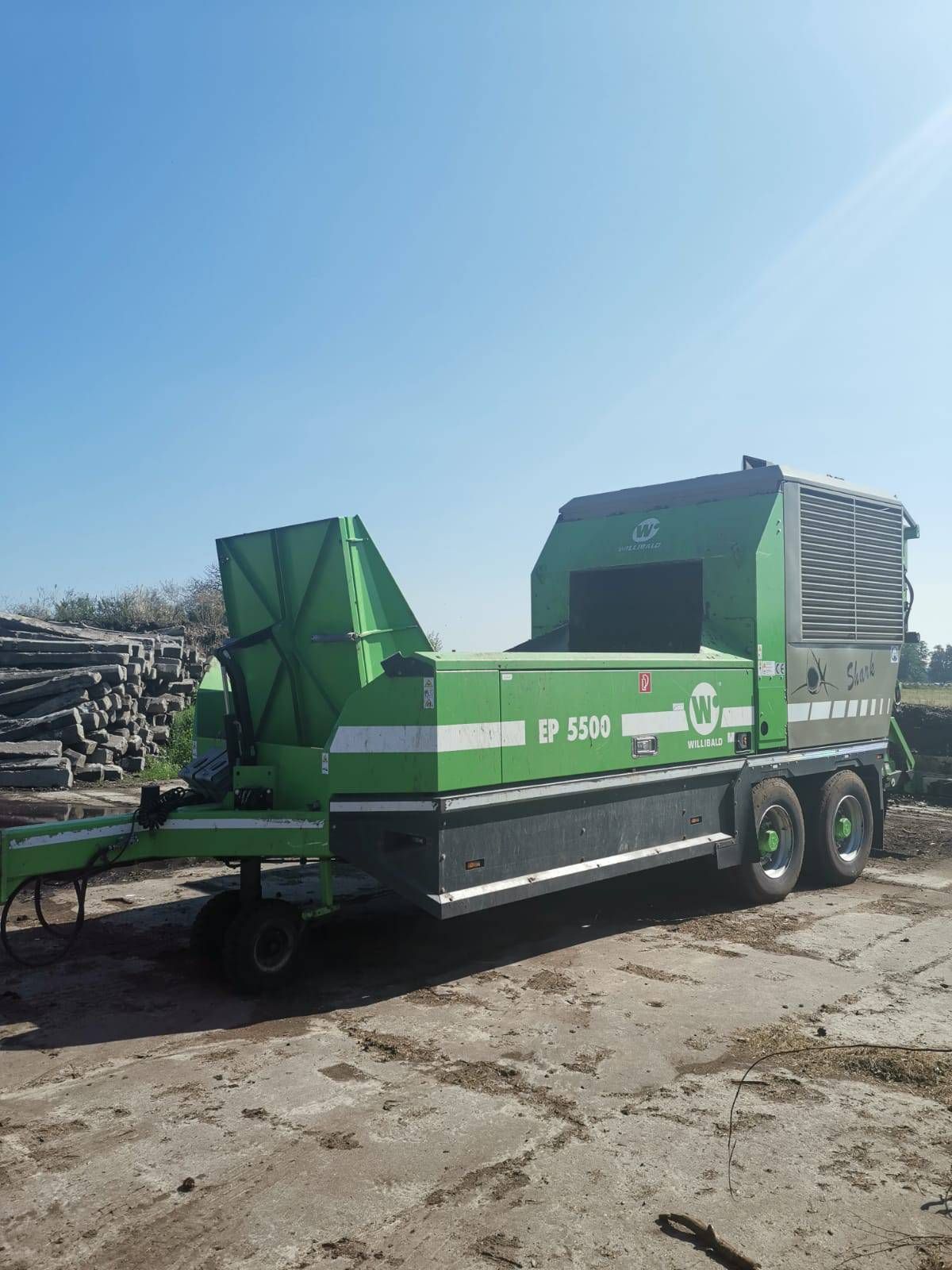 Ein grüner Schredder Anhänger steht auf einem unbefestigten Parkplatz.