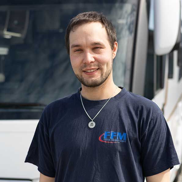 Ein Mann mit einem blauen Hemd und einer Halskette steht vor einem Bus.