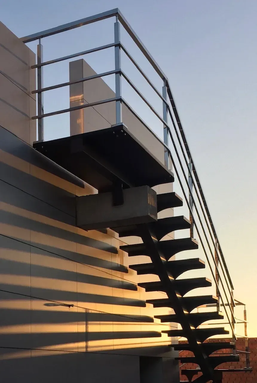 Escalera metálica exterior con barandillas al atardecer contra un cielo azul anaranjado.