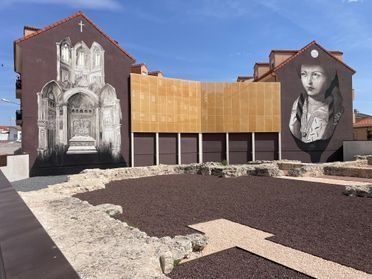 Edificio cubierto de murales junto a un pequeño patio con senderos de grava y ladrillo.