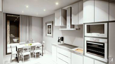 Cocina y comedor modernos de color blanco con horno empotrado, armarios y una pequeña mesa junto a la ventana.