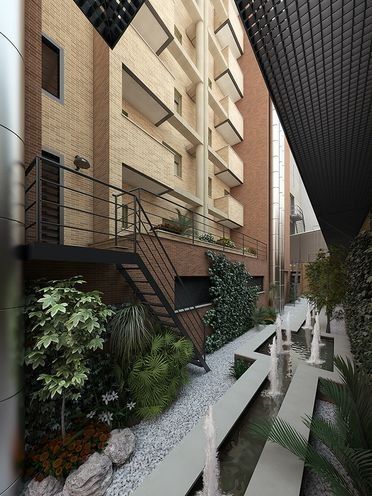 Patio interior de un moderno edificio de apartamentos con edificios de ladrillo, escaleras, vegetación y bancos blancos junto a una estrecha fuente de agua.
