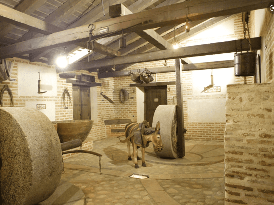 Interior de un molino histórico con vigas de madera, paredes de piedra y maquinaria antigua en exhibición.