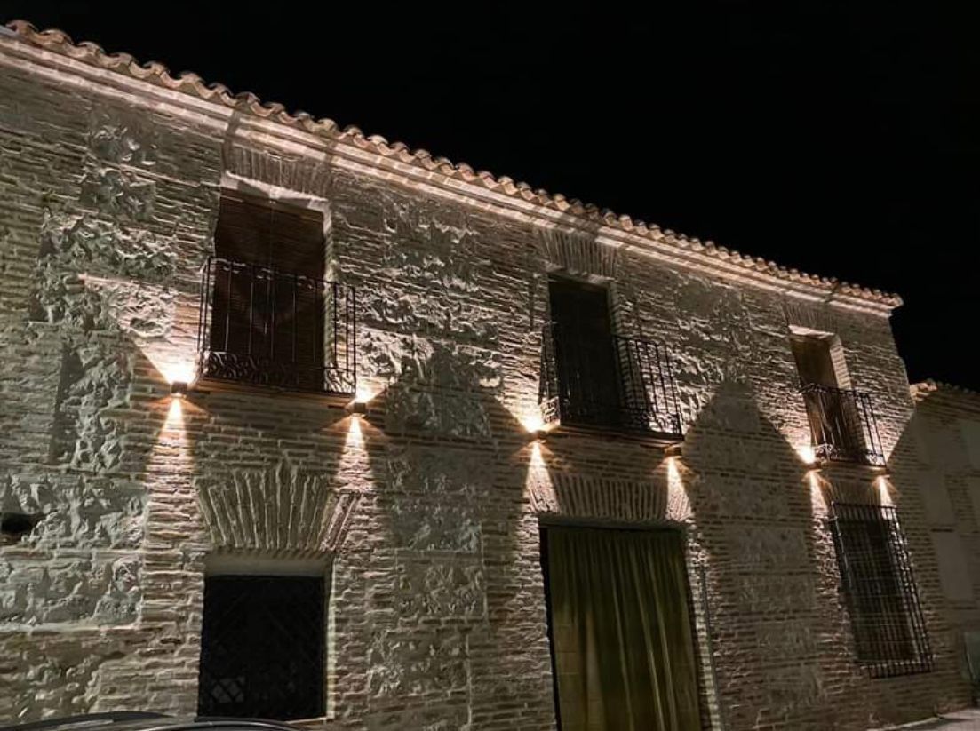 Fachada de piedra iluminada por la noche, con ventanas y una puerta central.