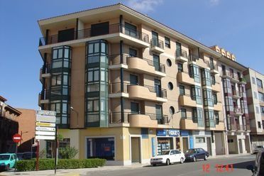 Edificio de apartamentos moderno con balcones y locales comerciales en la planta baja bajo un cielo azul despejado.