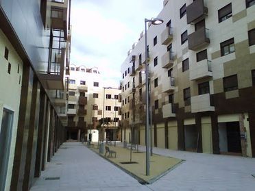 Patio de apartamentos moderno con balcones, pasillo estrecho y árboles jóvenes.