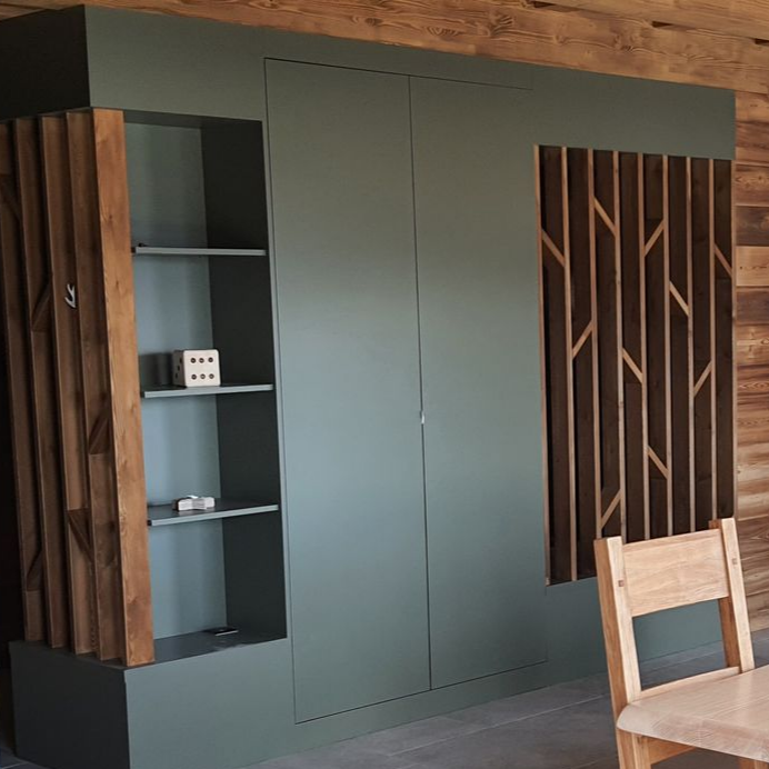 Armoire encastrée verte avec des accents en bois et des étagères ouvertes, adossée à un mur lambrissé de bois.
