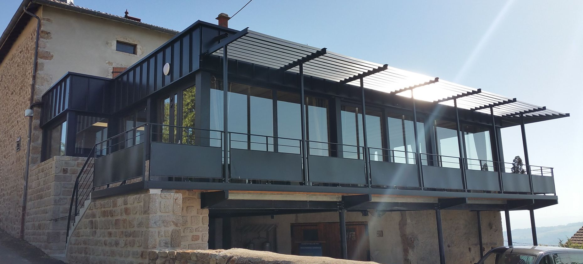 Une extension de bâtiment moderne en verre avec un toit en métal et un bâtiment en pierre.