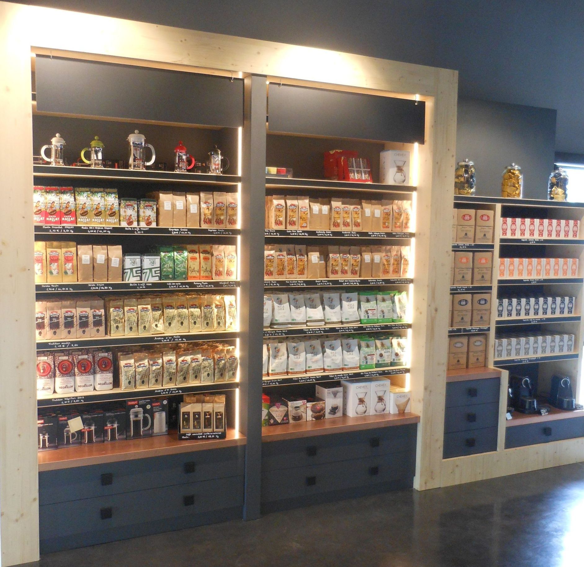 Étagères remplies de produits de café et de thé dans un magasin, encadrées de bois clair et d'accents bleu foncé.