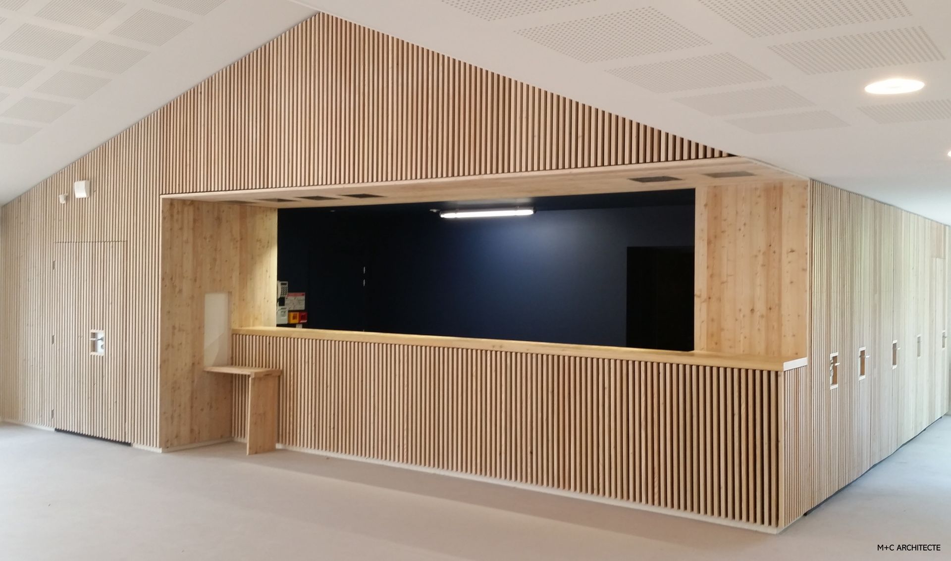 Comptoir en bois à l'intérieur sombre, encastré, à côté d'une série de portes en bois. Plafond blanc.