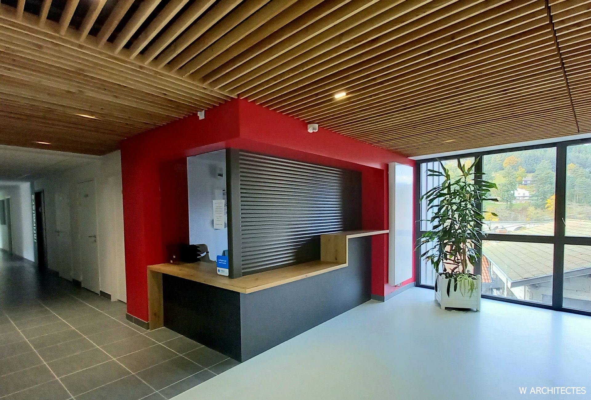 Espace de réception avec murs rouges, plafond en bois et comptoir aux tons noirs et boisés.