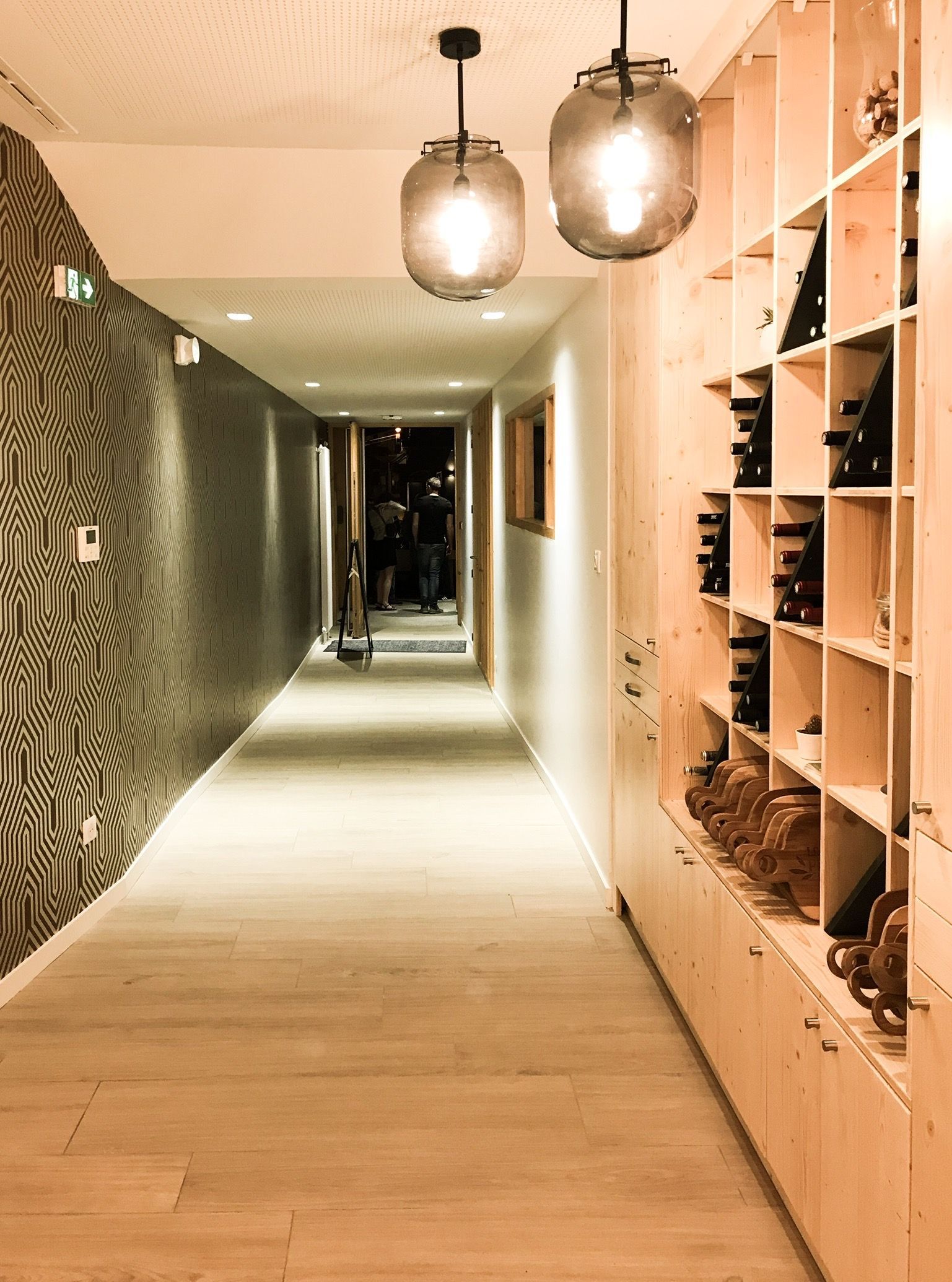 Couloir avec étagères en bois remplies de bouteilles de vin, papier peint à motifs et suspensions.
