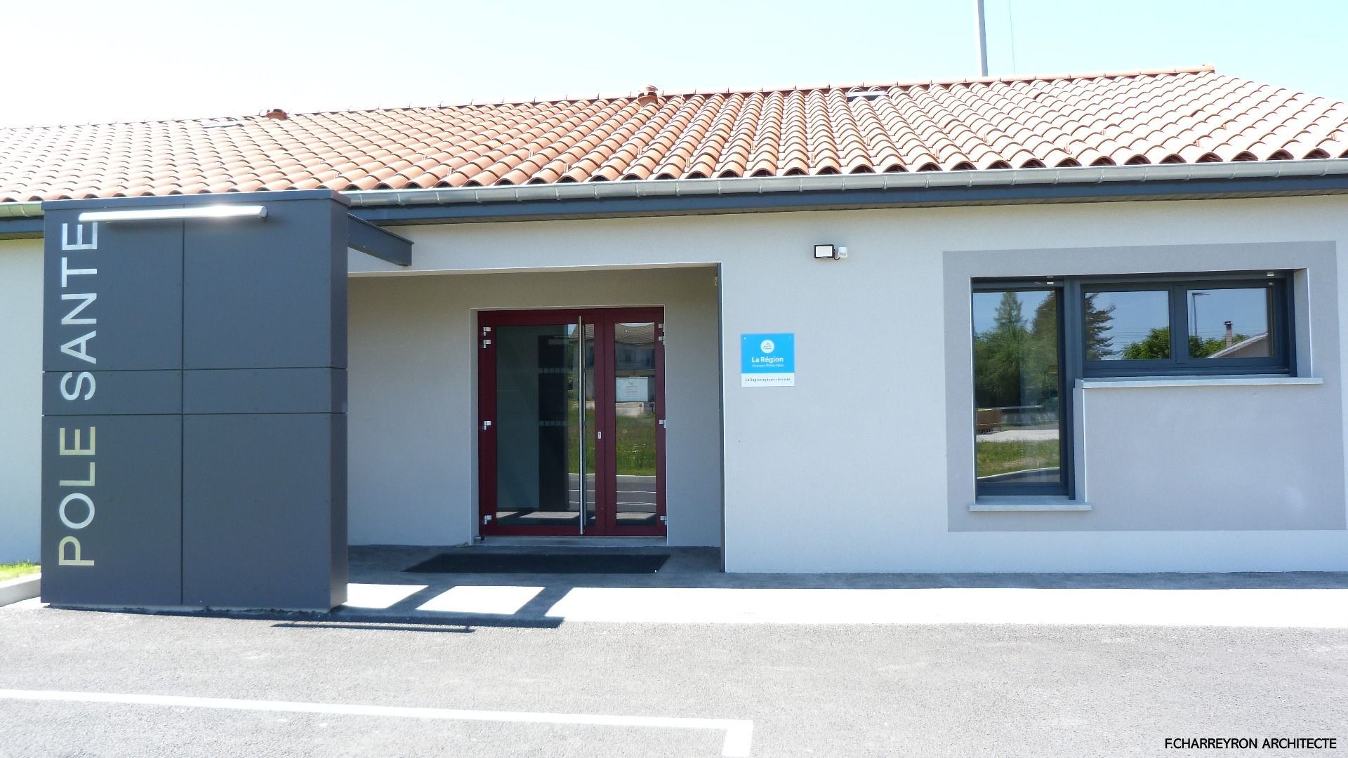 Vue extérieure d'un bâtiment de centre de santé gris clair ; entrée avec porte rouge foncé, panneau indiquant « POLE SANTE ».