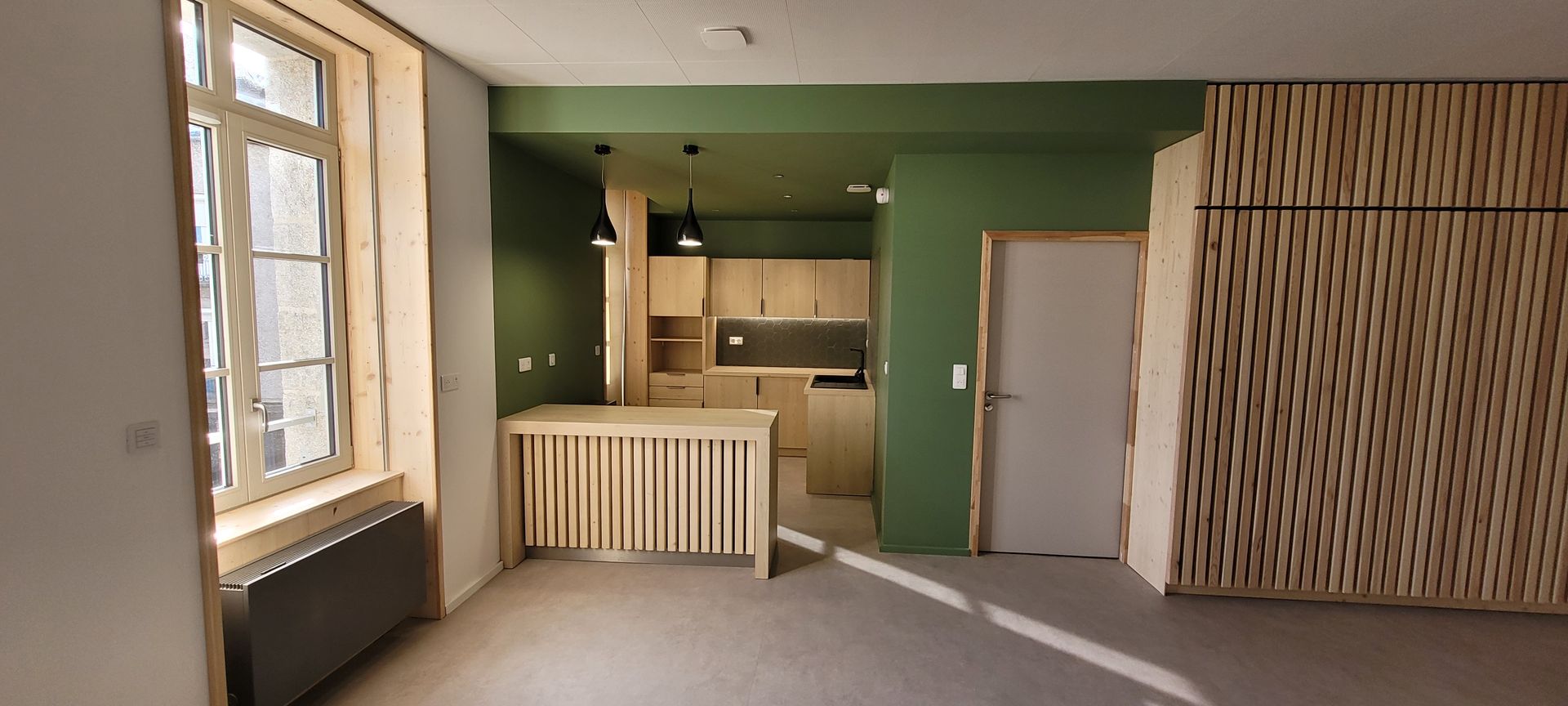 Intérieur d'une cuisine moderne avec des murs verts, des accents en bois et une grande fenêtre.