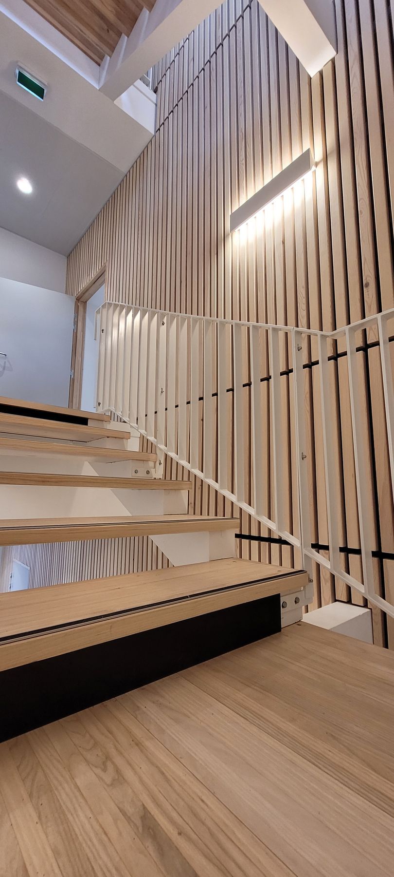 Escalier en bois avec rampe blanche et murs en panneaux de bois.