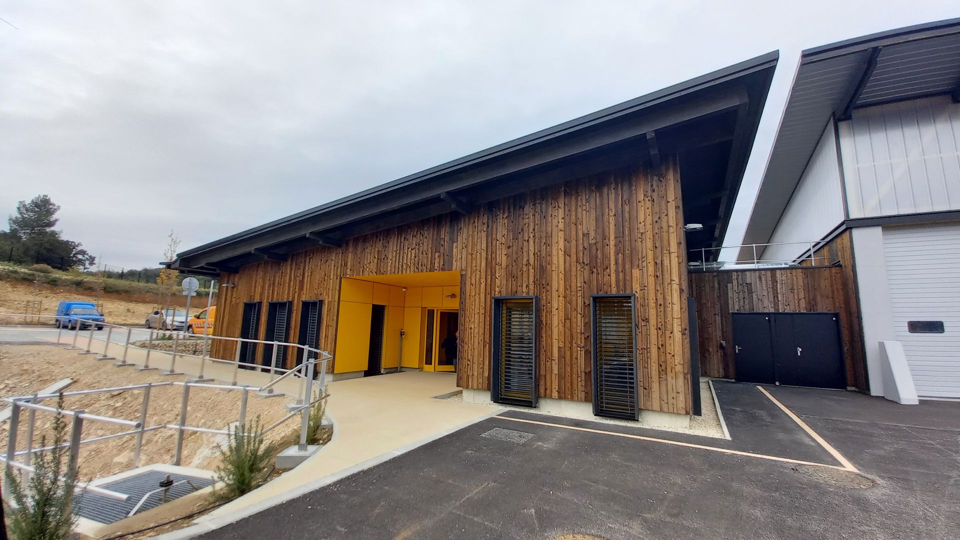 Vue extérieure d'un bâtiment moderne en bois avec une entrée jaune et un toit noir.