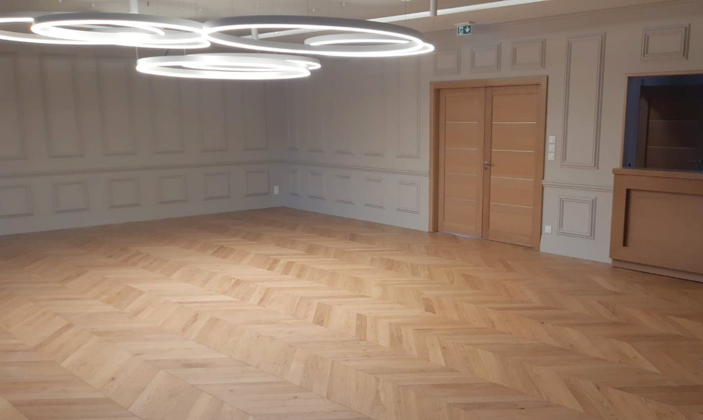 Pièce vide avec sol en chevrons en bois clair, murs lambrissés et plafonniers circulaires.