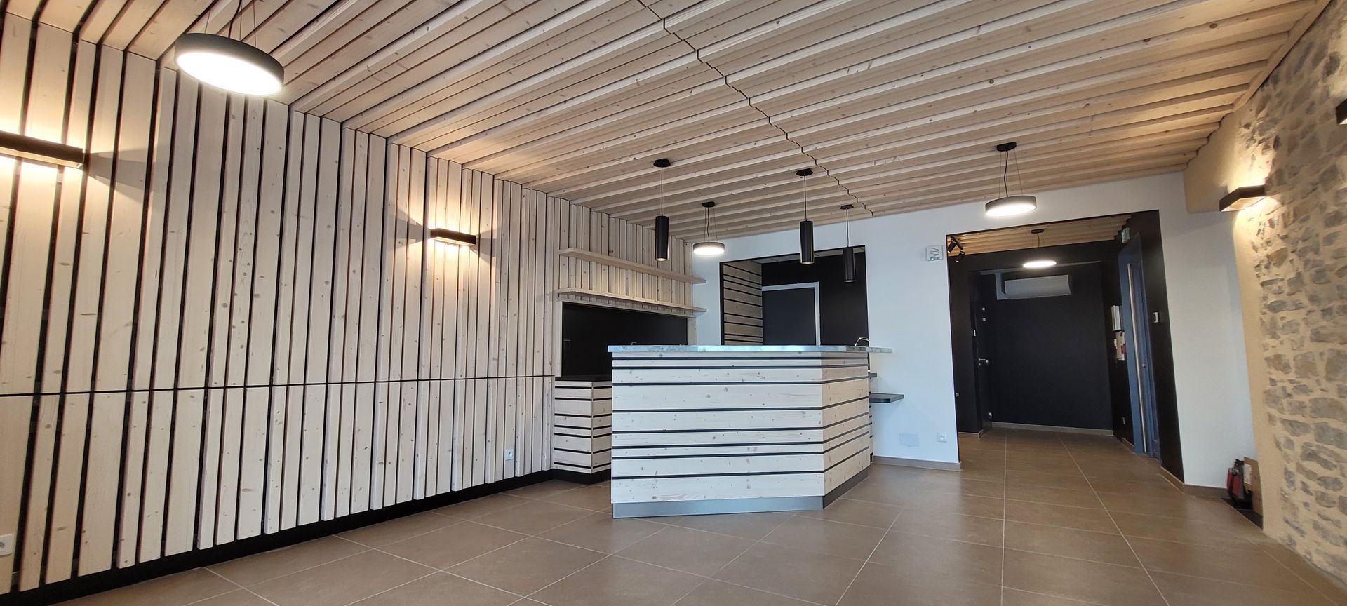 Intérieur moderne avec des accents de bois et des murs en pierre, probablement une zone de réception ou un café.