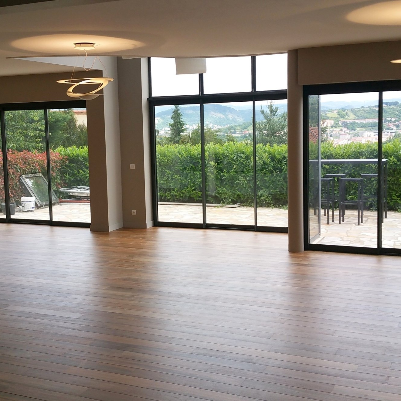 Chambre vide avec de grandes fenêtres donnant sur un paysage verdoyant, avec parquet.
