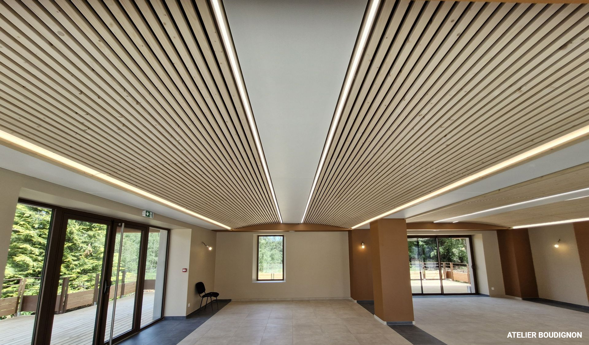 Plafond à lattes de bois avec éclairage encastré dans une grande pièce avec fenêtres et murs de couleur claire.