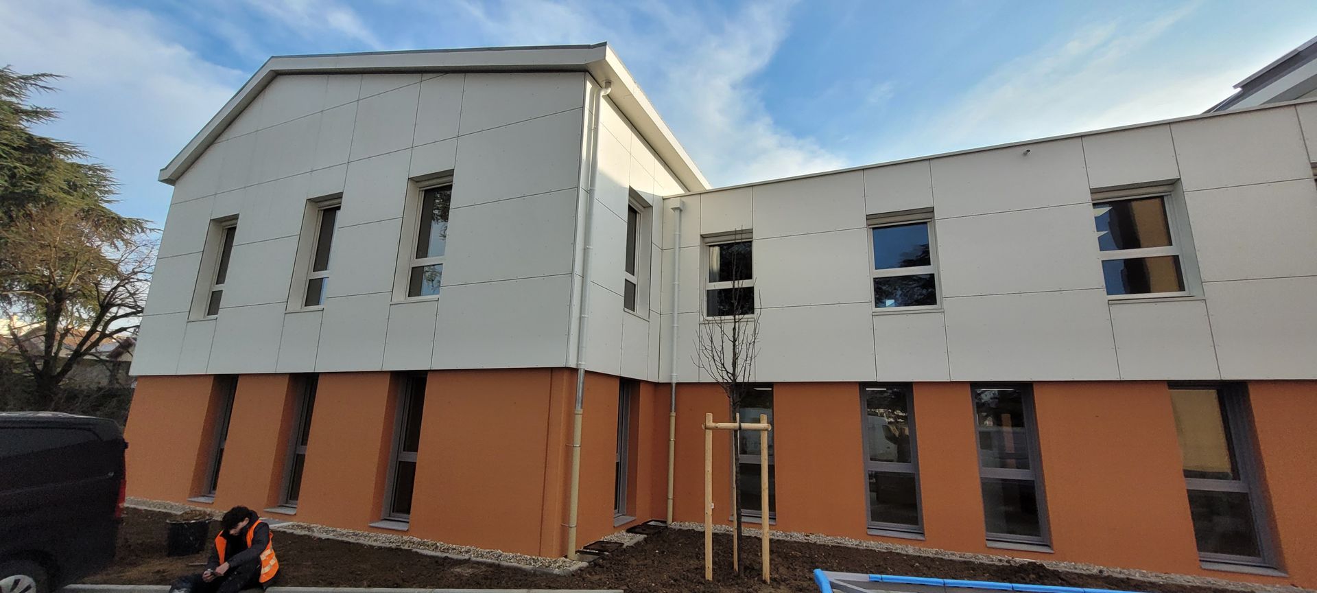 Bâtiment en construction, avec des murs supérieurs blancs et des murs inférieurs orange, avec un ciel bleu.