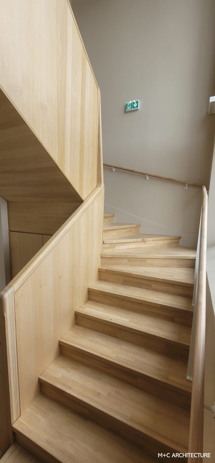 Escalier en bois avec des murs de couleur claire et un panneau de sortie.