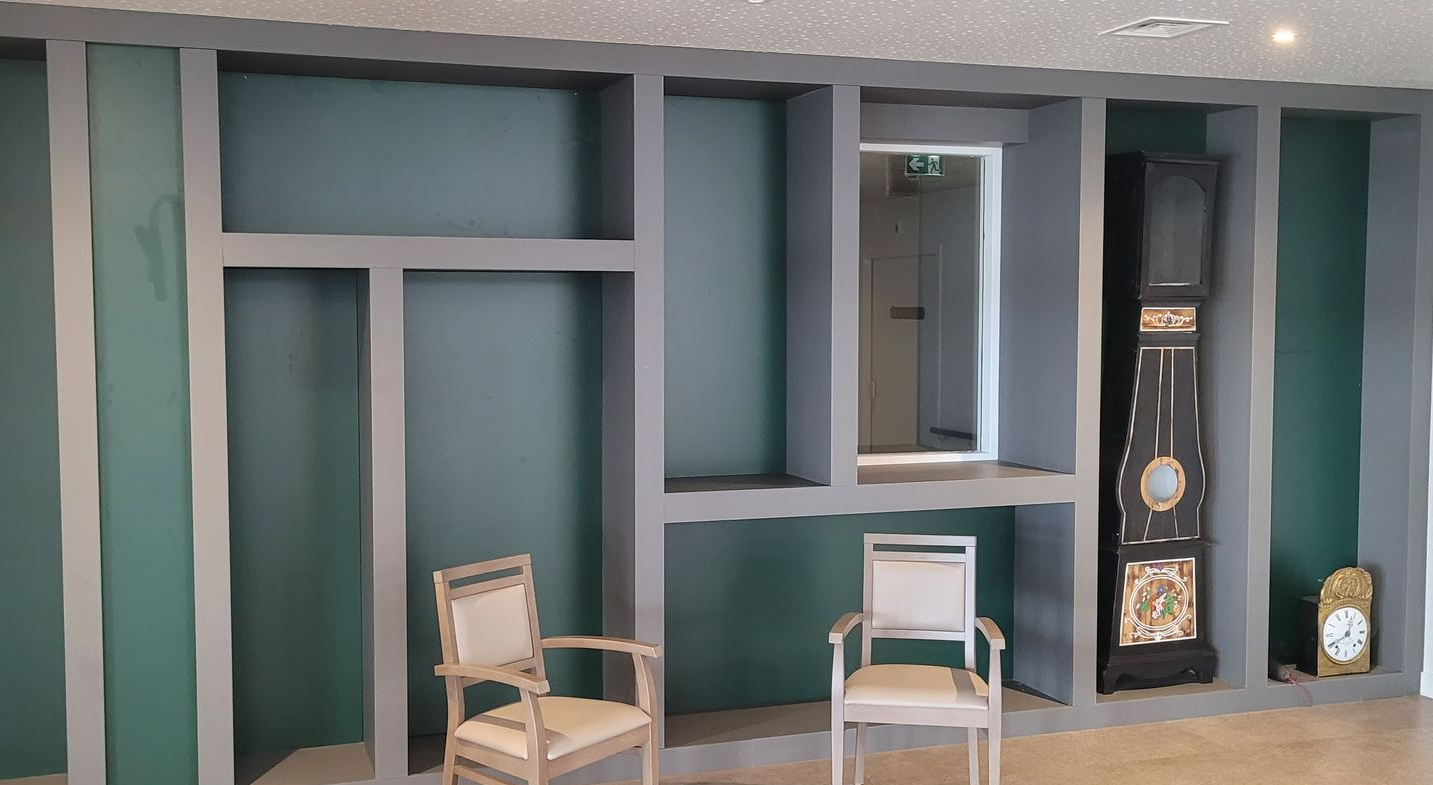 Deux chaises décorées font face à un meuble mural intégré avec des étagères, un mur végétal et une horloge grand-père.