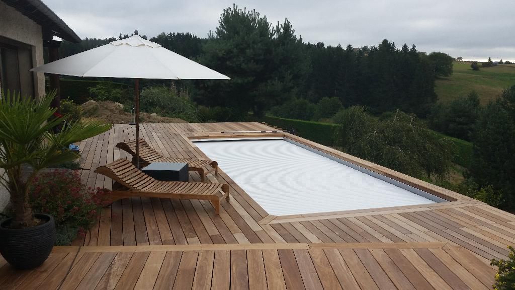 Terrasse en bois avec piscine, chaises longues, parasol et verdure.