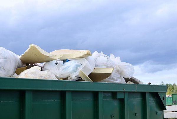 Un contenedor verde lleno de basura y espuma contra un cielo nublado.
