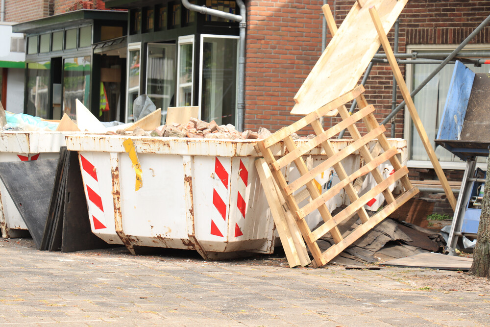 Un contenedor de basura con una paleta de madera frente a un edificio de ladrillos.