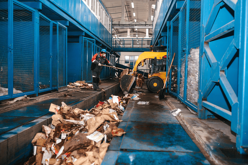 Un hombre está de pie junto a una carretilla elevadora amarilla en una fábrica.