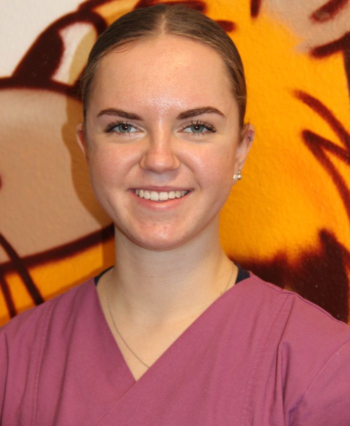 Junge Frau in rosa OP-Kleidung lächelt vor einem bunten Hintergrund in die Kamera.