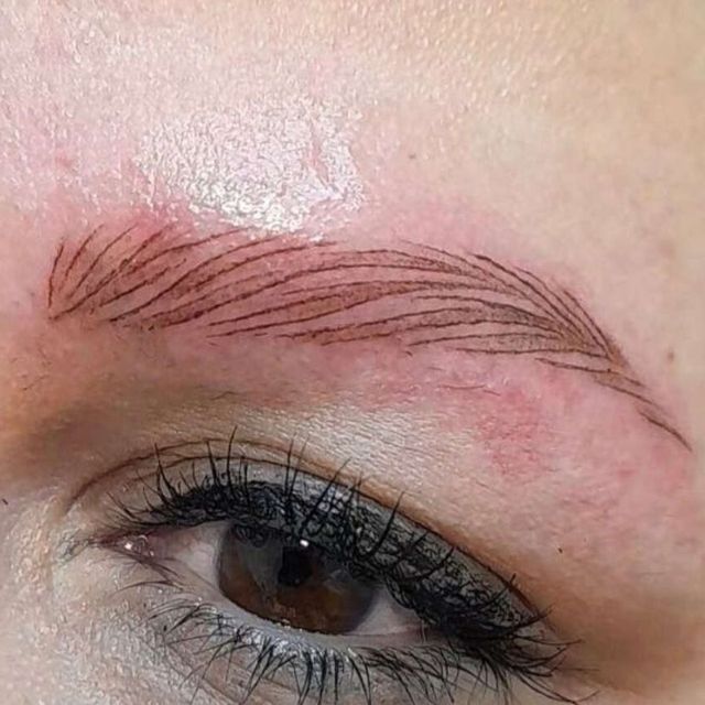 Primer plano de un ojo con cejas microblading. Trazos de tinta marrón imitan los pelos de las cejas.