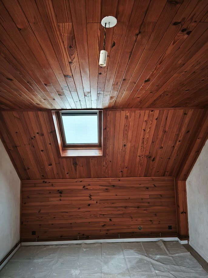 Pièce lambrissée avec puits de lumière. Plafond et murs en bois, murs blancs et luminaire suspendu.