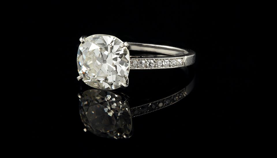Bague de fiançailles en argent sertie de diamants, avec une grosse pierre centrale taille coussin et un anneau pavé de diamants sur fond noir.