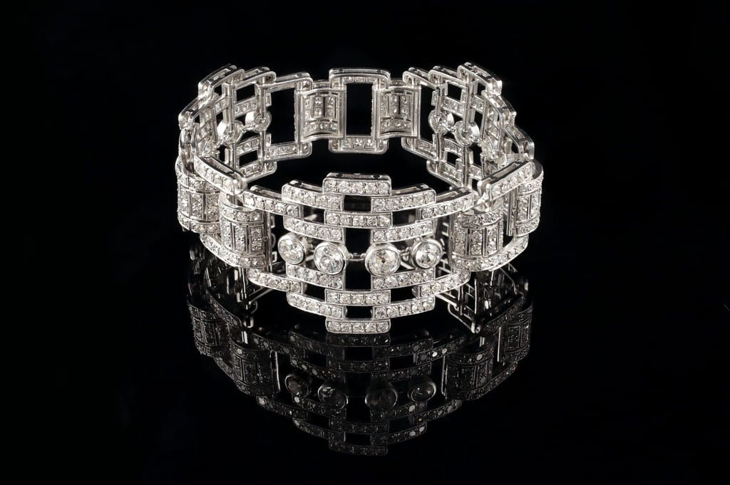 Un bracelet en argent à motif géométrique de diamants sur fond noir, se reflétant sur une surface miroir.