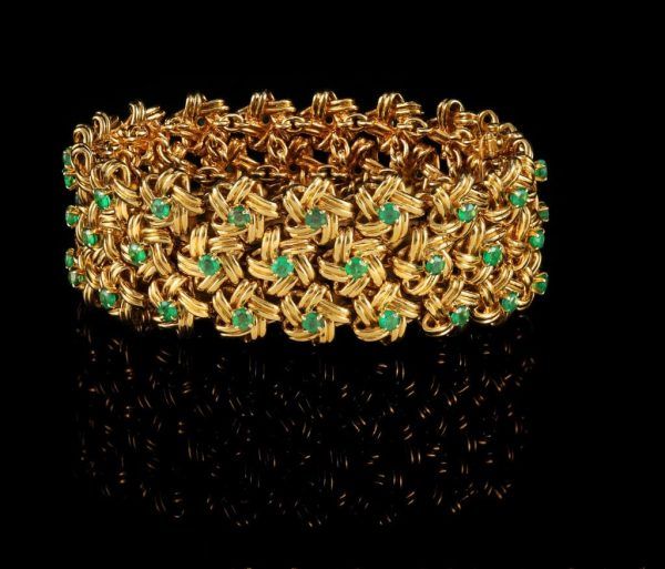 Bracelet en or composé de maillons floraux entrelacés ornés de petites pierres précieuses vertes, sur fond noir.