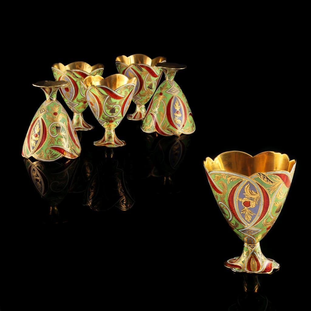 Six calices ornés, doublés d'or, avec des motifs floraux en émail vert, rouge et bleu disposés sur fond noir.