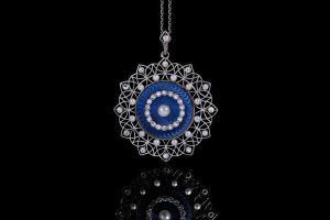Un pendentif circulaire complexe en filigrane d'argent, orné d'un centre en émail bleu, d'une perle et de diamants, monté sur une chaîne.