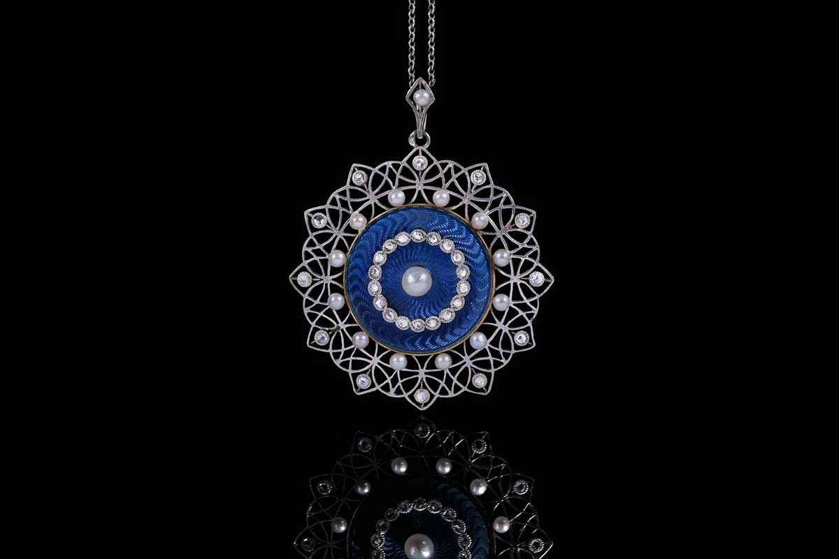 Pendentif en argent finement ouvragé, orné d'une perle centrale, d'émail bleu et de diamants sur fond noir.