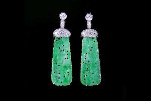 Une paire de boucles d'oreilles pendantes en jade vert, ornées de diamants, sur fond noir.