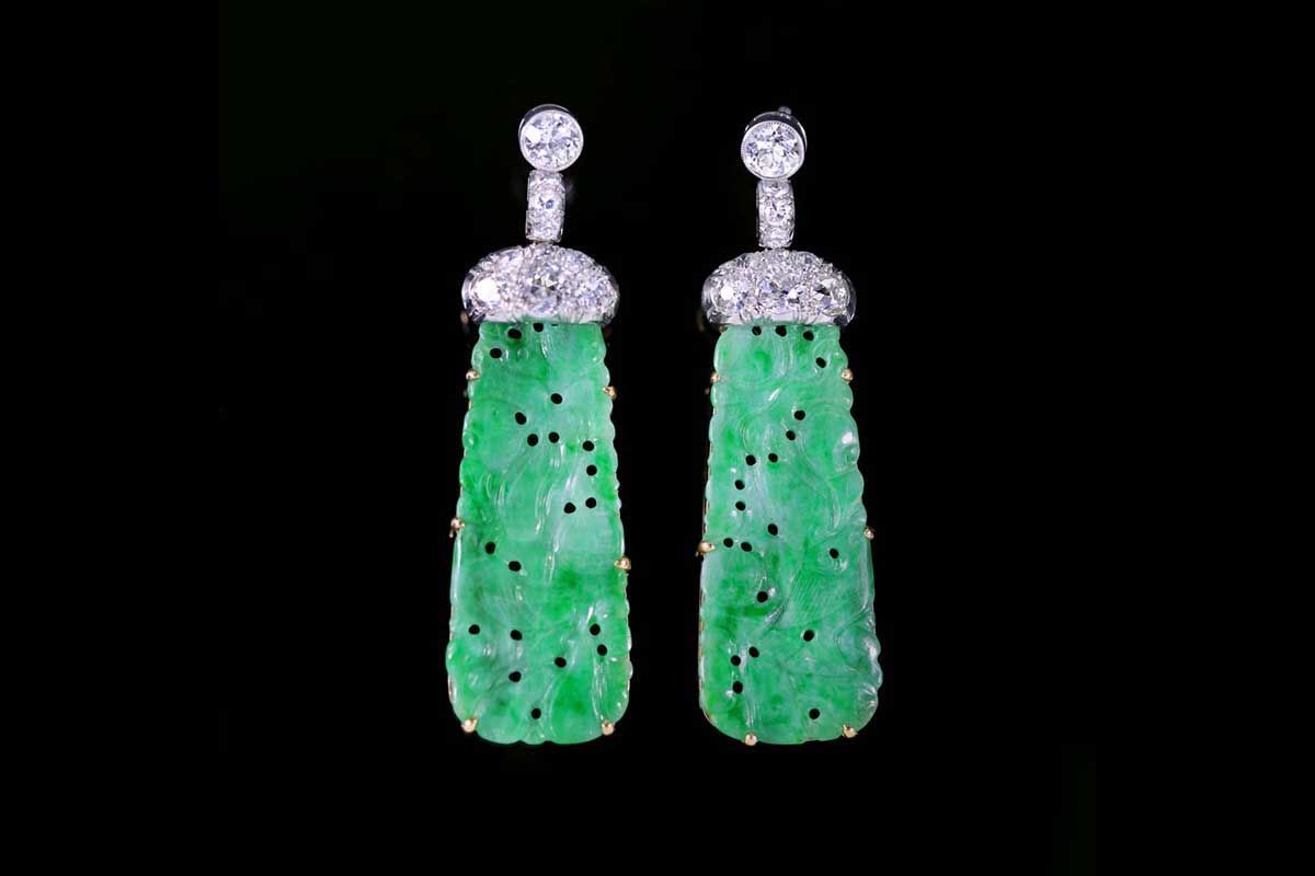 Une paire de boucles d'oreilles pendantes ornées de pendentifs en jade vert sculpté, sertis de diamants, sur fond noir.