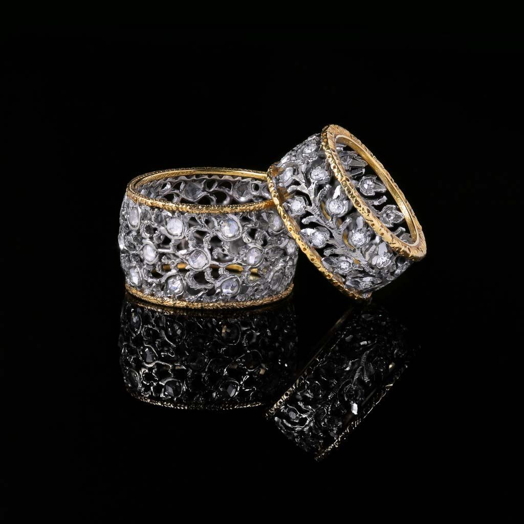 Deux bagues finement ouvragées, ornées de pierres scintillantes et de bords dorés, se détachant sur un fond noir aux reflets chatoyants.