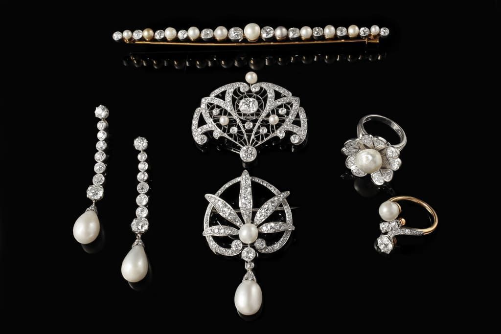 Une collection de bijoux anciens en diamants et perles, comprenant une broche, des boucles d'oreilles et des bagues, disposée sur un fond noir.